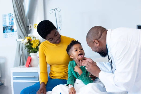 Afrikai Amerikai Férfi Orvos Vizsgálja Fiú Beteg Száját Anyával Kórházban — Stock Fotó