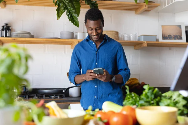 幸せなアフリカ系アメリカ人男性の台所で夕食を調理 スマートフォンを使用して 自宅だけで質の高い時間を過ごす — ストック写真