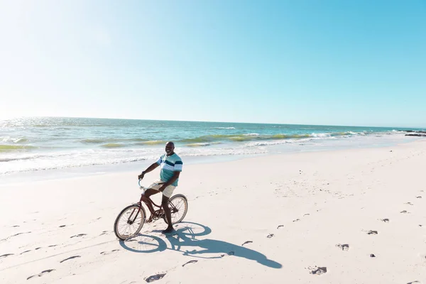 アフリカ系アメリカ人の老人は 晴れた日に砂浜で海と澄んだ空に自転車に乗っています コピースペース 変更されていない 楽しみ 自然とアクティブなライフスタイル — ストック写真