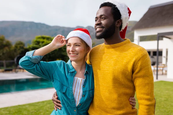 サンタの帽子を抱いて屋外で立ってクリスマスを祝う幸せな多様なカップルのイメージ クリスマス お祝い 包括性とライフスタイルの概念 — ストック写真