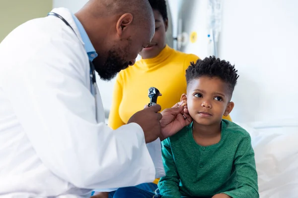 アフリカ系アメリカ人男性医師は 男性患者の耳を母親と一緒に調べるためにオートスコープを使用している 医療サービス — ストック写真