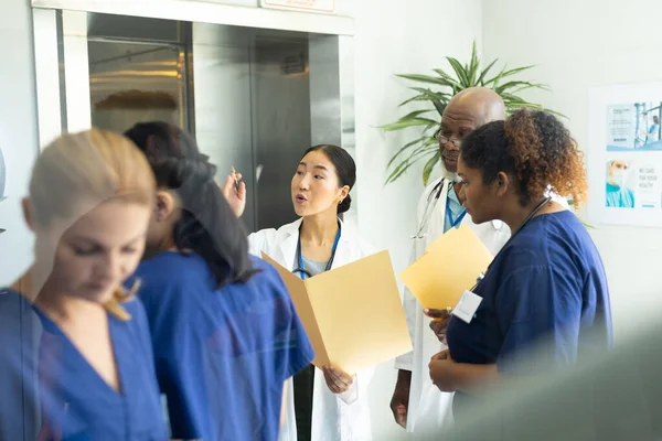 忙しい病院の廊下で議論するファイルを保持する男性と女性の医師の多様なグループ 医療サービス — ストック写真