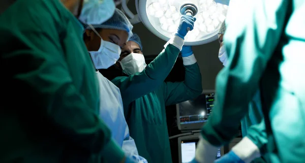 Tecnologia Cirúrgica Masculina Biracial Ajustando Luz Para Colegas Durante Operação — Fotografia de Stock