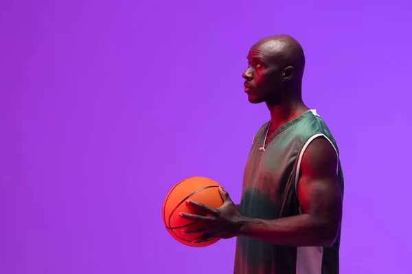 Image of african american basketball player with basketball on neon purple background. Sports and competition concept.