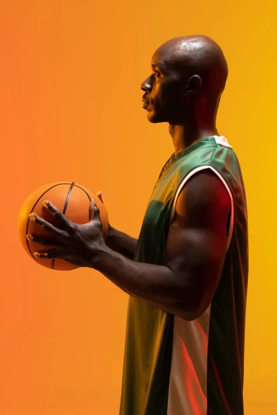 ネオンオレンジの背景にバスケットボールを持つアフリカ系アメリカ人のバスケットボール選手のイメージ スポーツ 競技の概念 — ストック写真