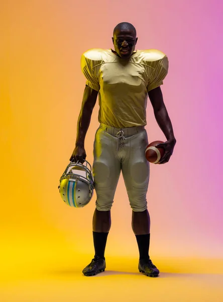 Американский Футболист Африканского Происхождения Держит Мяч Неоновым Желтым Фиолетовым Освещением — стоковое фото