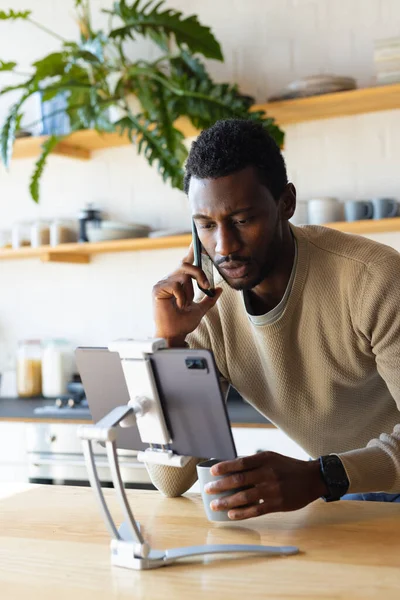快乐的非洲裔美国人靠在厨房的台面上 用平板电脑和智能手机聊天 独自在家度过高质量的时光 — 图库照片