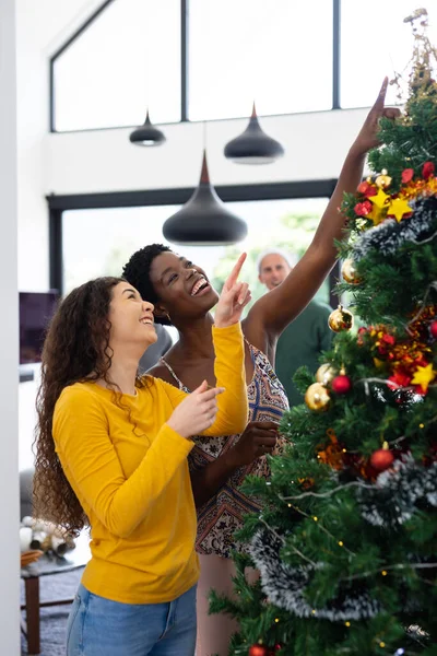 ツリーを見て家でクリスマスを祝う2人の幸せな多様な女性の友人の垂直画像 クリスマス お祝い 包括性とライフスタイルの概念 — ストック写真