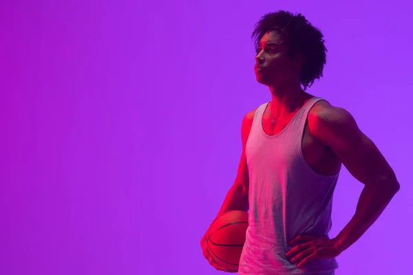 Image of biracial basketball player with basketball and copy space on neon purple background. Sports and competition concept.