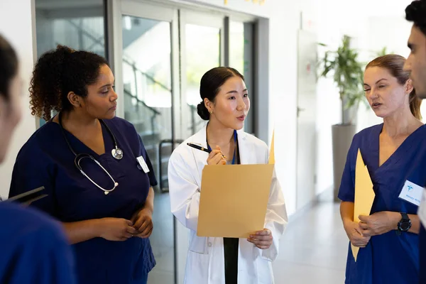 病院の廊下で多様な同僚と話してフォルダを持つアジアの女性医師 医療サービス — ストック写真