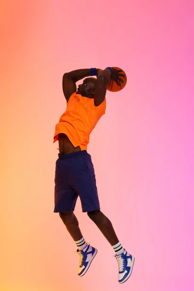 非洲裔美国篮球员在粉色至橙色背景下与篮球一起跳跃的图片 体育和竞争概念 — 图库照片