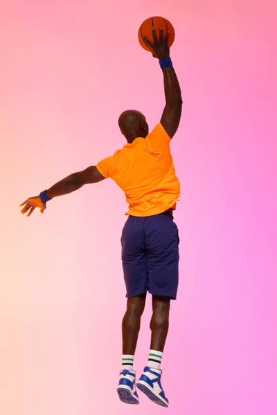 ピンクのバスケットボールでオレンジの背景にジャンプするアフリカ系アメリカ人バスケットボール選手のイメージ スポーツ 競技の概念 — ストック写真