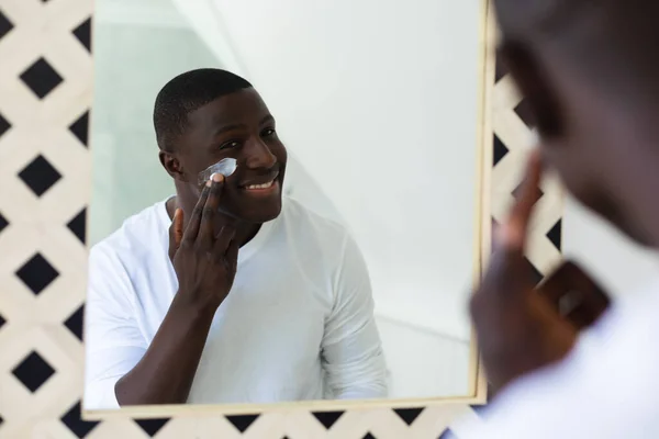Usmívající Afroameričan Který Aplikuje Hydratační Krém Obličej Zrcadla Koupelně Inkluzivita — Stock fotografie