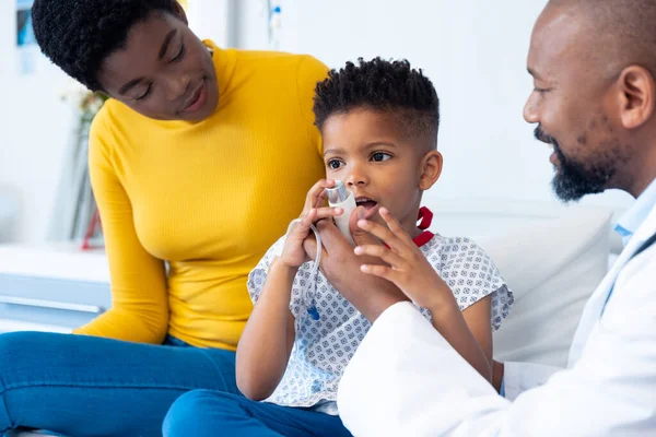 非裔美国男性医生给男孩看吸入器 母亲在医院里 医疗和保健服务 — 图库照片