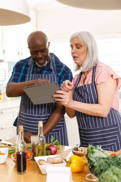Happy Senior Diverse Couple Wearing Aprons Using Tablet Kitchen Spending — Stock Photo, Image