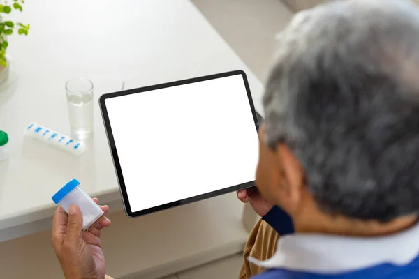 Senior Biracial Man Sitting Table Holding Medicine Bottle Using Tablet — Stock Photo, Image