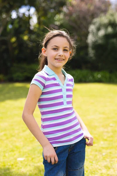 縞模様のTシャツを着て庭に立っている若い白人の少女の垂直肖像画 概念外で過ごす時間 — ストック写真