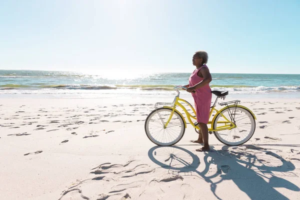 澄んだ空に対して砂浜に立って自転車でアフリカ系アメリカ人のシニア女性の側面図 コピースペース 変更されていない 楽しみ 自然とアクティブなライフスタイル — ストック写真