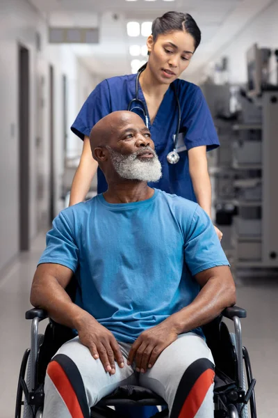 不同的女医生在走廊将老年男病人推倒在轮椅上 复制空间 医疗和保健服务 — 图库照片