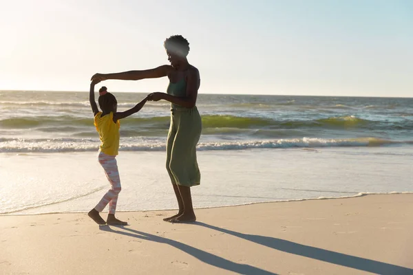 アフリカ系アメリカ人の母親は娘の手を取り合い 日没時に澄んだ空に対して海岸で踊る コピースペース 変更されていない 一緒に 子供時代 楽しさと自然コンセプト — ストック写真