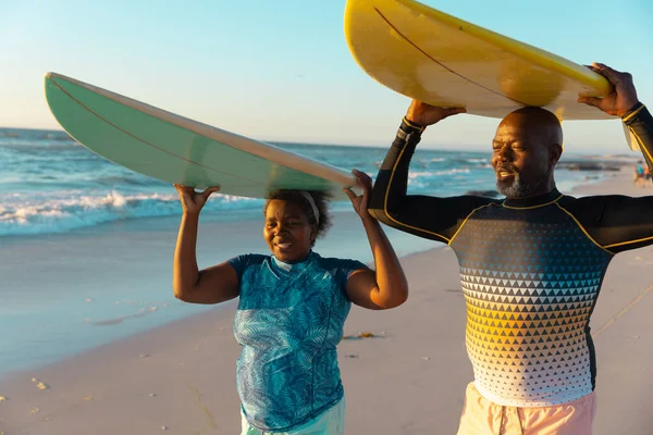 アフリカ系アメリカ人の高齢者のカップルは 空に対してビーチに立っている間 頭の上にサーフボードを運ぶ コピースペース ウォータースポーツ レクリエーション 変更なし 一緒に 楽しさ — ストック写真