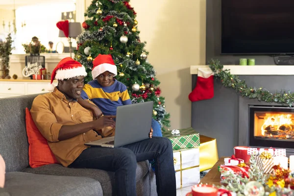 非洲裔美国人的父亲和儿子坐在沙发上 使用笔记本电脑 圣诞节 家庭时间和采用技术概念的庆祝活动 — 图库照片