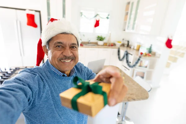 Sorrindo Homem Biracial Sênior Santa Chapéu Segurando Presente Natal Durante — Fotografia de Stock