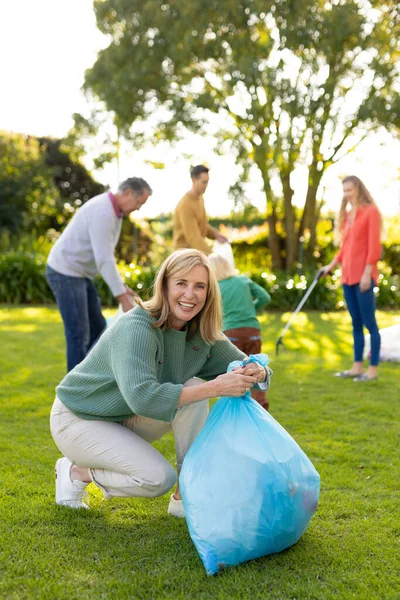 一个快乐的高加索女人带着垃圾袋在花园里的垂直形象 回收和生态意识概念 — 图库照片