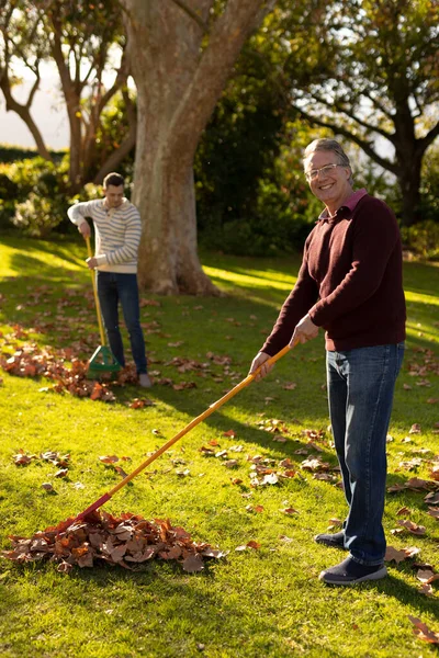 정원에서 나뭇잎을 까딱거리는 코카서스 아버지 와성인 아들의 모습을 수직적으로 것이다 — 스톡 사진