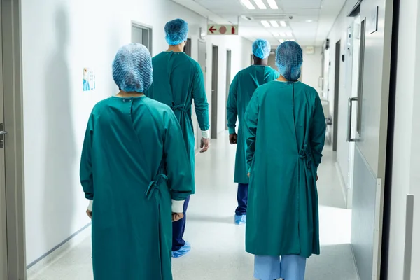 外科用キャップの4人の外科医の背面ビューと病院の廊下を歩いてガウン 医療サービス — ストック写真