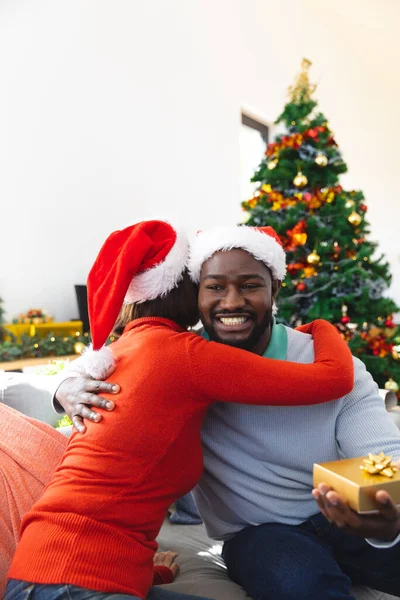Casal Diverso Feliz Vestindo Chapéus Papai Noel Sentado Sofá Desempacotando — Fotografia de Stock