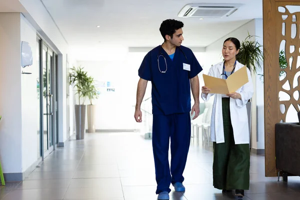 不同的男医生和女医生与文件夹讨论步行在医院走廊 与复制空间 医疗和保健服务 — 图库照片