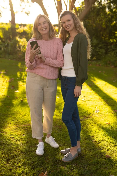 秋季花园中快乐的高加索母亲和成年女儿在镜头前摆姿势的垂直图像 家庭与共同度过美好时光的概念 — 图库照片