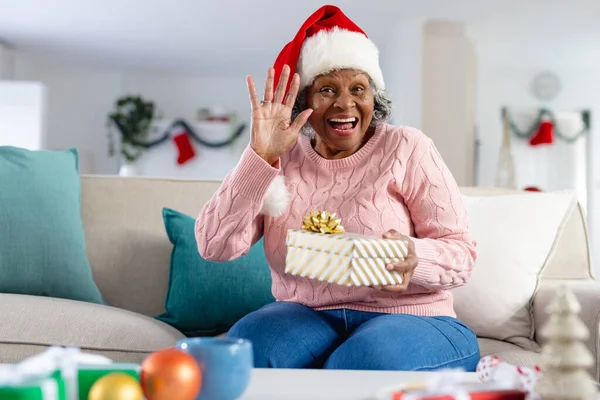 快乐的资深非洲裔美国女人戴着圣塔克洛斯帽 挥挥手 独自呆在家里 利用技术 — 图库照片