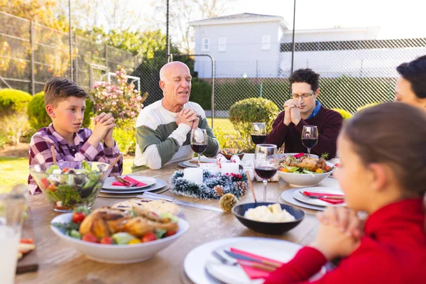 Happy caucasian family spending time together and praying before meal in the garden. Spending time together outside.