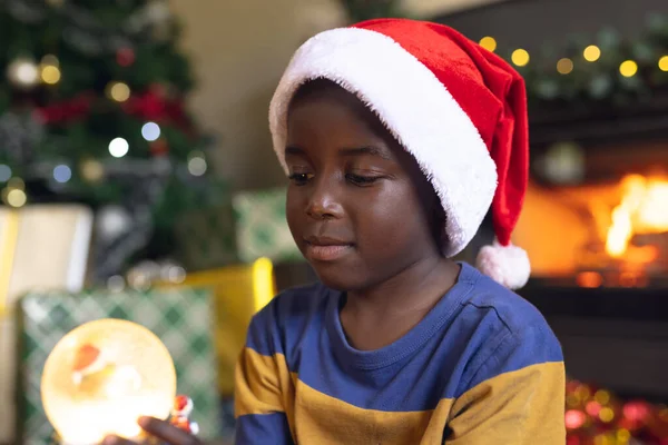 快乐的非洲裔美国男孩拿着圣诞雪球坐在旁边的壁炉边 圣诞节 童年和庆祝概念 — 图库照片