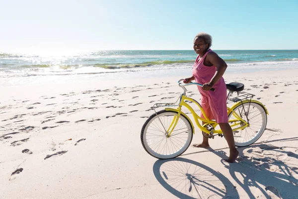 澄んだ空を背景に砂浜に自転車で立つアフリカ系アメリカ人のシニア女性 コピースペース 変更されていない 楽しみ 自然とアクティブなライフスタイル — ストック写真