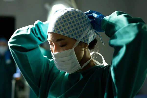 Asian female surgeon in surgical cap and gown tying mask in operating theatre. Hospital, medical and healthcare services.