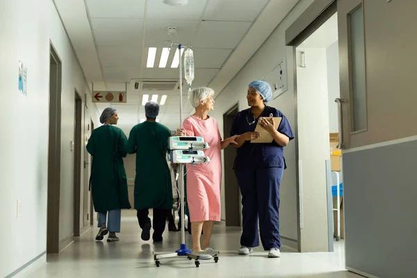 Szczęśliwa Zróżnicowana Lekarka Pacjentka Biegunem Kroplówki Rozmawiająca Zatłoczonym Szpitalnym Korytarzu — Zdjęcie stockowe