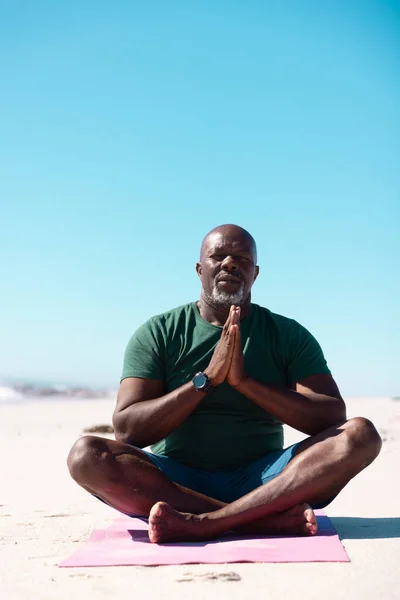 澄んだ青い空の下で アフリカ系アメリカ人の老人が足を組んでビーチで瞑想しています コピースペース 変更されていない アクティブなライフスタイル — ストック写真