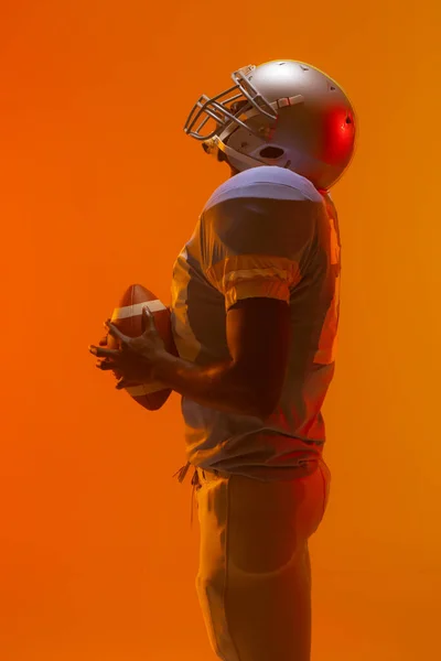 Amerykański Amerykański Futbolista Trzymający Piłkę Neonowym Pomarańczowym Oświetleniem Sport Ruch — Zdjęcie stockowe