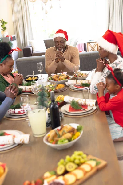 クリスマスの食事をする前に祈るアフリカ系アメリカ人の家族の垂直写真 クリスマス 家族の時間とお祝いの概念 — ストック写真