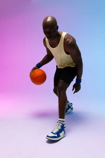 Image of african american basketball player with basketball on neon purple to blue background. Sports and competition concept.