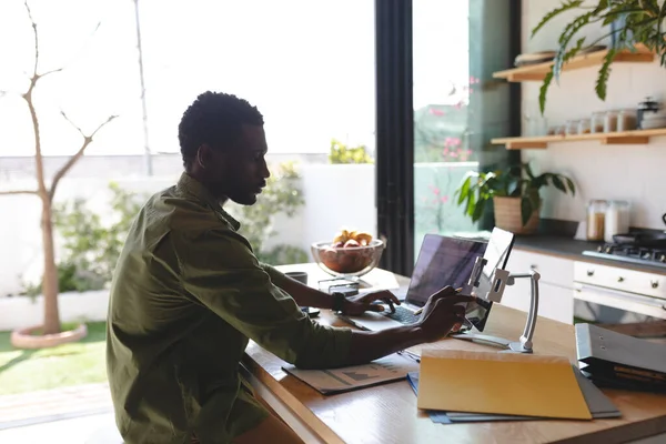 幸せなアフリカ系アメリカ人の男性の台所でノートパソコンやタブレットを使用して座っている 自宅だけで質の高い時間を過ごす — ストック写真