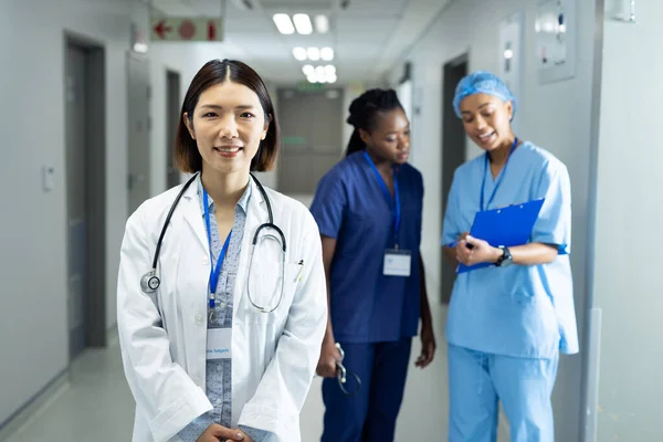 医院走廊里笑容满面的亚裔女医生的画像 背景中的同事 医疗和保健服务 — 图库照片
