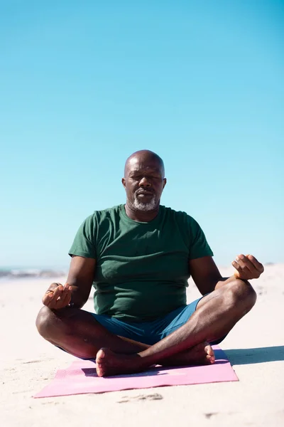 アフリカ系アメリカ人のはげの老人は 澄んだ青い空に対してビーチでマットに足を瞑想しています コピースペース 変更されていない 休暇とアクティブなライフスタイル — ストック写真