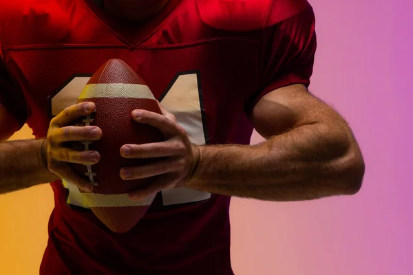 Midsection of caucasian male american football player with neon purple and yellow lighting. Sport, movement, training and active lifestyle concept.