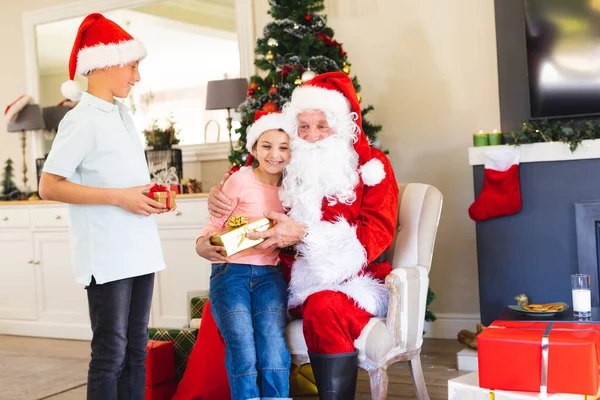 サンタクラスの白人の子供たちはクリスマスプレゼントを与えます クリスマス 家族の時間とお祝いの概念 — ストック写真