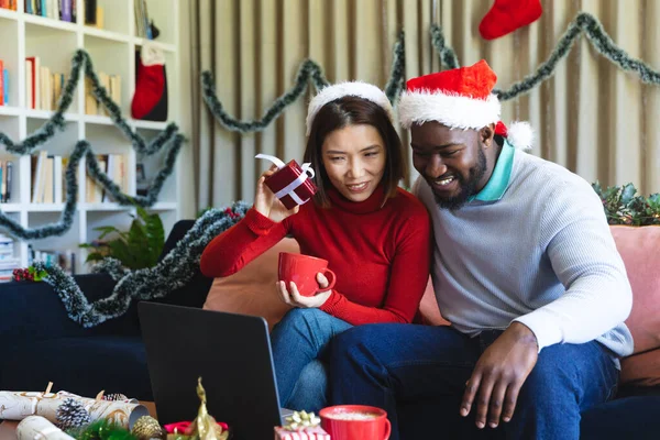 快乐多样的夫妇戴着圣塔克洛斯帽 使用笔记本电脑进行视频通话 在圣诞佳节一起共度美好时光 — 图库照片