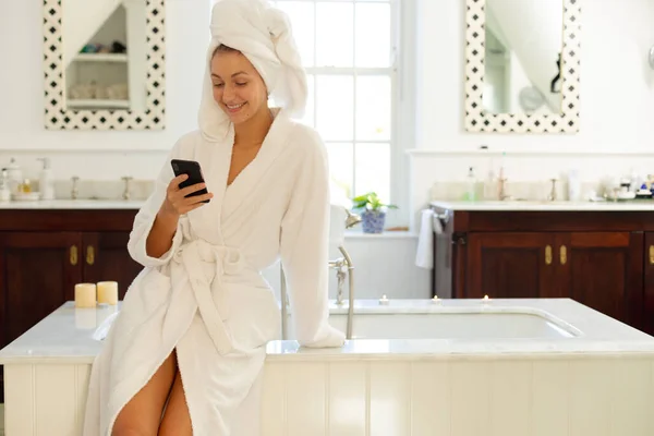 快乐的高加索女人穿着长袍 在浴室里用智能手机 独自在家度过美好时光 — 图库照片